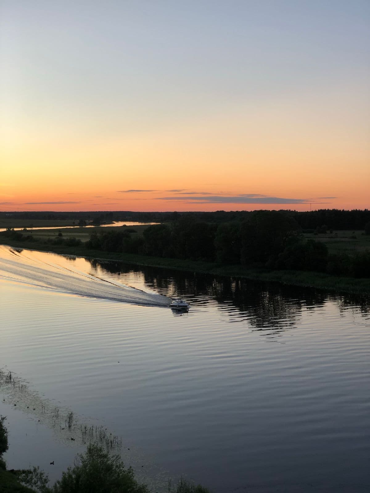 Petit bateau sur une rivière au crépuscule, ciel orange et reflets